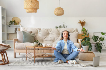 Wall Mural - Young woman with headphones meditating on carpet in living room