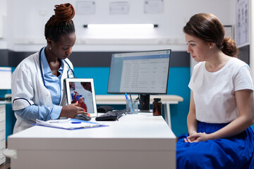 Wall Mural - Cardiac doctor specialist showing heart chart on tablet to patient during checkup appointment. Cardiologist in modern clinic office presenting diagnostic and treatment information to woman