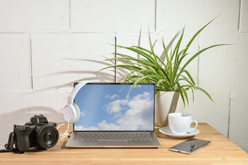 Wall Mural - Laptop, camera, headphones and smart phone on a wooden desk, office workplace of a journalist or photographer against a white painted wall, copy space