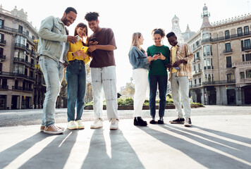 Young group of people having fun using cell phones together outside. Millennial student friends sharing social media content on mobile phone app standing in city street. Technology concept.