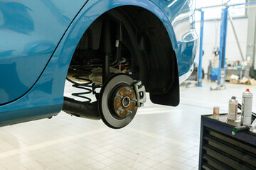 Lifted car without wheel waiting for repair in service station. Working area with automobile on high lift at vehicle repair shop. Concept of service center in process of car maintenance