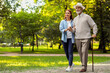 © New Africa - Senior man with walking cane and young woman in park. Space for text