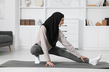 Wall Mural - Muslim woman in hijab stretching on fitness mat at home