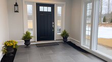 A Photo Of The Front Entryway Of A House With A Black Door, White Walls, And Gray Tile Flooring.