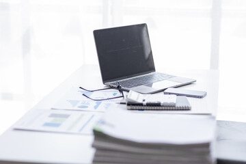 Wall Mural - Laptop Computer, notebook, and eyeglasses sitting on a desk in a large open plan office space after working hours	