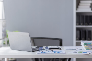 Wall Mural - Laptop Computer, notebook, and eyeglasses sitting on a desk in a large open plan office space after working hours	