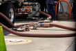© F Armstrong Photo - Gasoline being offloaded from a tanker truck into an underground storage tank at a gas station. A worker is in the background