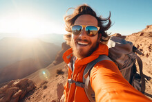 Happy Young Man Hiker Taking Selfie On Top Of Mountain, Smiling Tourist With Backpack And Glasses Enjoying Beautiful Sunset From The Top Of Mountain