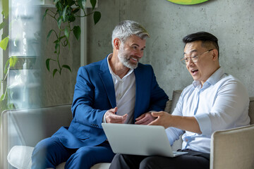 Wall Mural - Business men sitting on sofa in modern office talking together and using laptop.