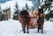 Two Children Ride On A Retro Sleigh With Horses In Winter Time. Mountain Snowy Landscape Background. Tours, Horse Riding.