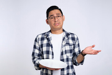 Confused young Asian man in casual shirt holding empty blank plate isolated on white background