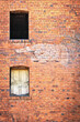 Side of an old brick building with two windows, one empty and one boarded, with a faded old sign of a finger pointing