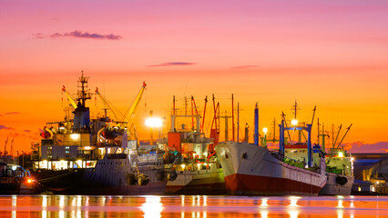 Group of fishing boats and oil tanker ship dock at port for unloading in the riverside industrial area against colorful twilight sky background