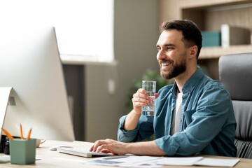 Handsome young businessman drinking water and working on computer in office