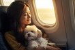 Young woman holding a small dog on her lap while sitting by airplane window. Travelling with pets in the cabin.