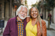 © Sabrina - Multiracial senior couple smiling on camera during city trip vacation with street in background