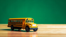 Yellow School Bus Model On The Student Table With Chalkboard Or Blackboard Background. Transportation And Education Concept.