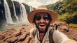 Handsome tourist visiting national park taking selfie picture in front of waterfall - Traveling life style concept with happy man wearing hat and sunglasses enjoying freedom in the nature
