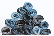 © TanyaJoy - Pyramid of rolled up denim jeans on a white background. Trendy denim clothing, shopping, fashion, consumption.
