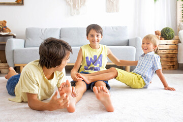 Wall Mural - Happy positive children, tickling on the feet, having fun together, boy brothers at home having wonderful day of joy