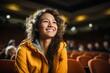 Eine lächelnde Studentin mit dunklen Haaren und gelber Jacke sitzt im Auditorium oder Hörsaal in der Universität und hört sich interessiert und glücklich die Vorlesung an