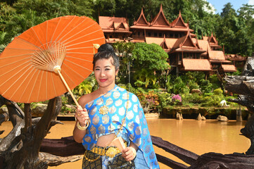 Beautiful Asian woman in Thai National costume holds a paper umbrella posing for photos at a Thai house.