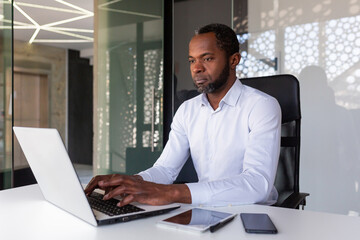 Serious focused african american programmer working inside office, man coding new software on laptop, mature experienced team leader developing technical project.