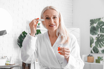 Wall Mural - Mature woman applying under-eye cream in bathroom