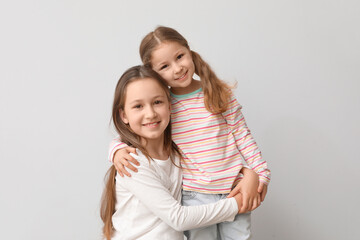 Wall Mural - Cute little sisters hugging on light background