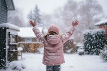 In A Suburban Backyard, A Young Child, Bundled Up In Colorful Winter Attire, Stands With Arms Outstretched, Trying To Catch The Delicate Snowflakes