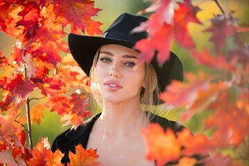 Beautiful girl outdoors in autumn fall. Young woman collects yellow fall leaves in autumn. Beauty woman holds autumn yellow leaf fall the face. Portrait of sensual woman over autumn fall background.