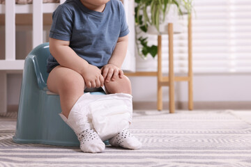 Little child sitting on plastic baby potty indoors, closeup. Space for text