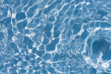 Blue water with ripples on the surface. Defocus blurred transparent blue colored clear calm water surface texture with splashes and bubbles. Water waves with shining pattern texture background.