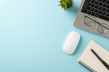 Office essentials arrangement. Top view of laptop, mouse, notepad, pen, flowerpot, glasses on pastel blue backdrop. Empty area for text or promotions