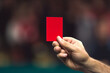Realistic photo in low saturation of a referee wearing black raising a red card in a soccer match