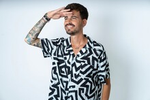 young caucasian man wearing printed shirt very happy and smiling looking far away with hand over head. Searching concept.