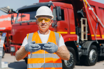 Concept banner automated logistics online internet. Dump truck driver man in uniform with tablet computer controls loading of cargo or coal