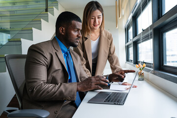 Two happy business woman and man using laptop working on computer at workplace. Cheerful young professional multiethnic colleagues team discussing online digital technology corporate project in office