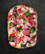 Pizza with salami, ham, vienna sausages, kalamata, olives, broccoli, pelati, pesto. Roman pizza rectangular on dark background