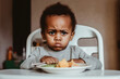 Cute displeased black kid with a plate of delicious food. Refusal of children from food.