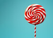 Christmas lollipop isolated over light blue background, copy space. New year candy icon with spiral red and white stripes and swirls. Round peppermint hard sugar candy, Xmas and New Year sweet gift