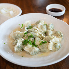 Wall Mural - Fresh, delicious boiled garlic chives dumplings, jiaozi in white plate on wooden table background.