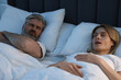 Irritated man lying near his snoring wife in bed at home