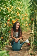 Wall Mural - Blue colored watering can. Little girl is in the garden with tomatoes