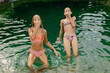 Two friends swim in the lake in swimsuits and dabble with water