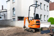 Small orange crawler excavator at a construction site near a residential building.