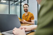 © LIGHTFIELD STUDIOS - bearded businessman with envelopes smiling near blurred colleague typing on laptop in office