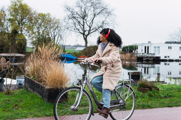 Poster - Young happy woman riding a bike while listening music in town