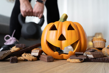 Wall Mural - Woman exercising at home. Focus on Halloween pumpkin and chocolate sweets. Seasonal fit diet choice. Rejecting unhealthy food. Fitness gym workout training. Staying in shape during autumn fall season.