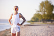 Portrait of beautiful smiling woman jogger in sport clothes and sunglasses on beach. Woman relaxing, resting after morning fitness routine.